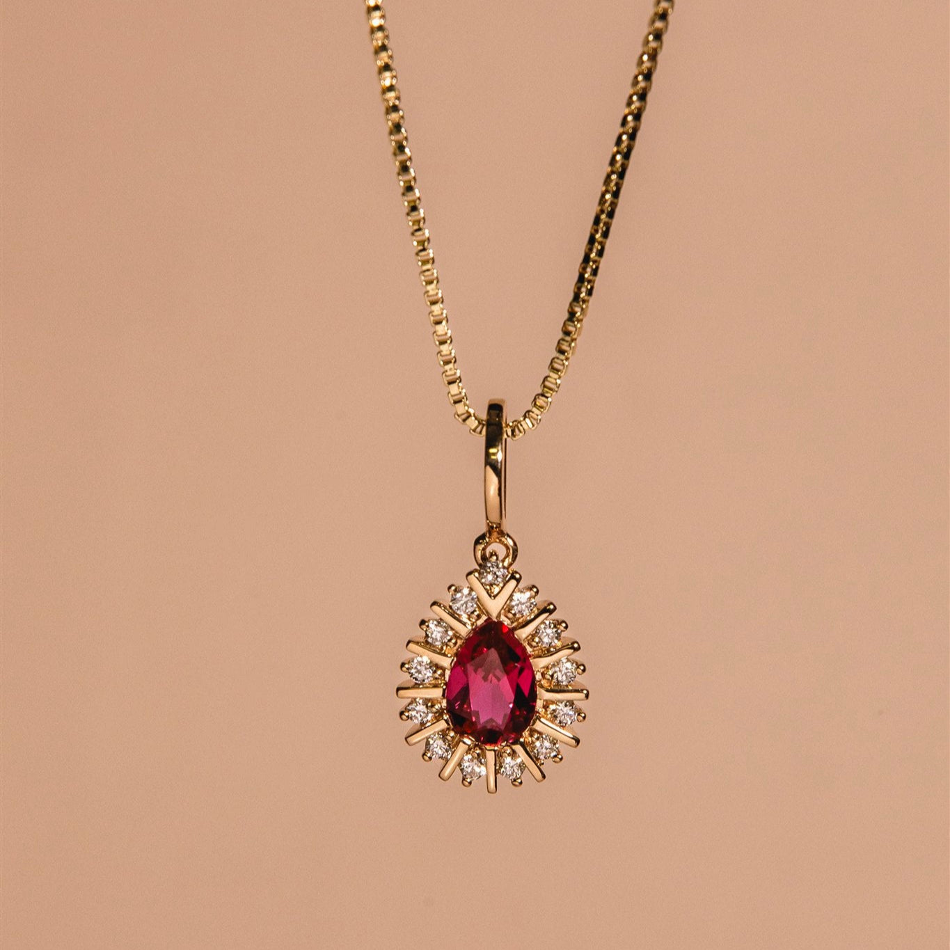 Gold necklace with a red gemstone pendant on a beige background