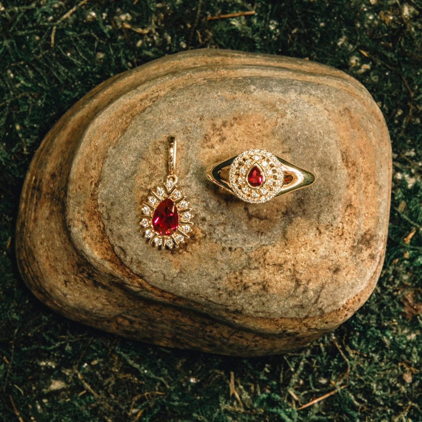Gold ring with red gemstone and matching earring on a textured stone surface.