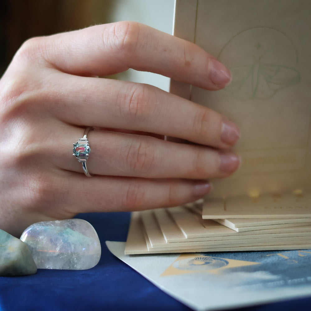 Hand wearing a ring holding ritual cards with an angel aura quartz and blue surface