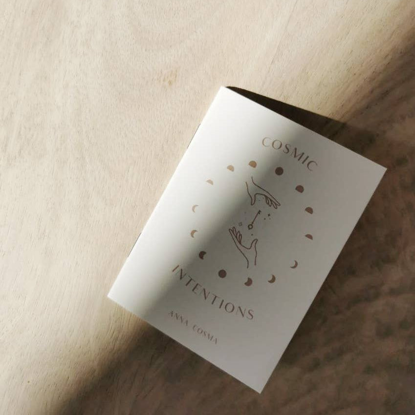 White book titled 'Cosmic Intentions' by Anna Cosmos on a wooden surface