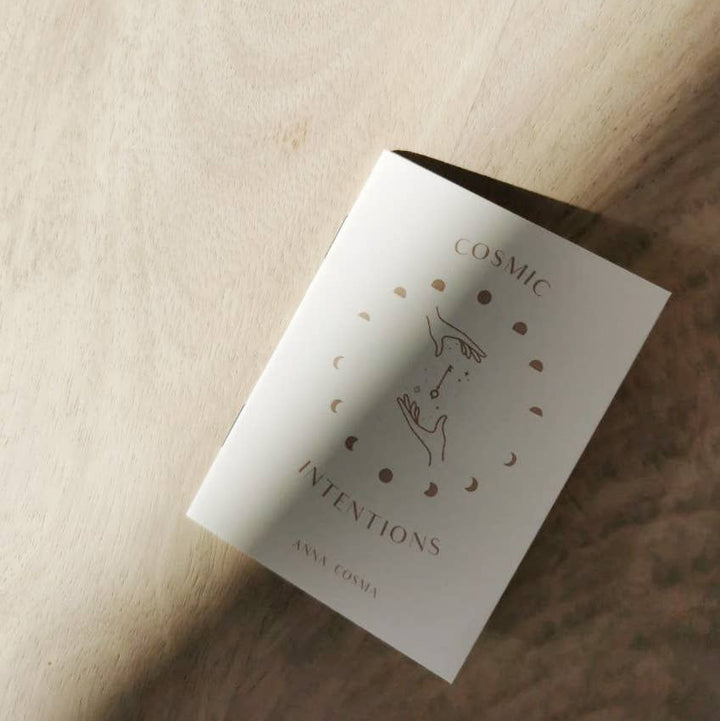 White book titled 'Cosmic Intentions' by Anna Cosmos on a wooden surface