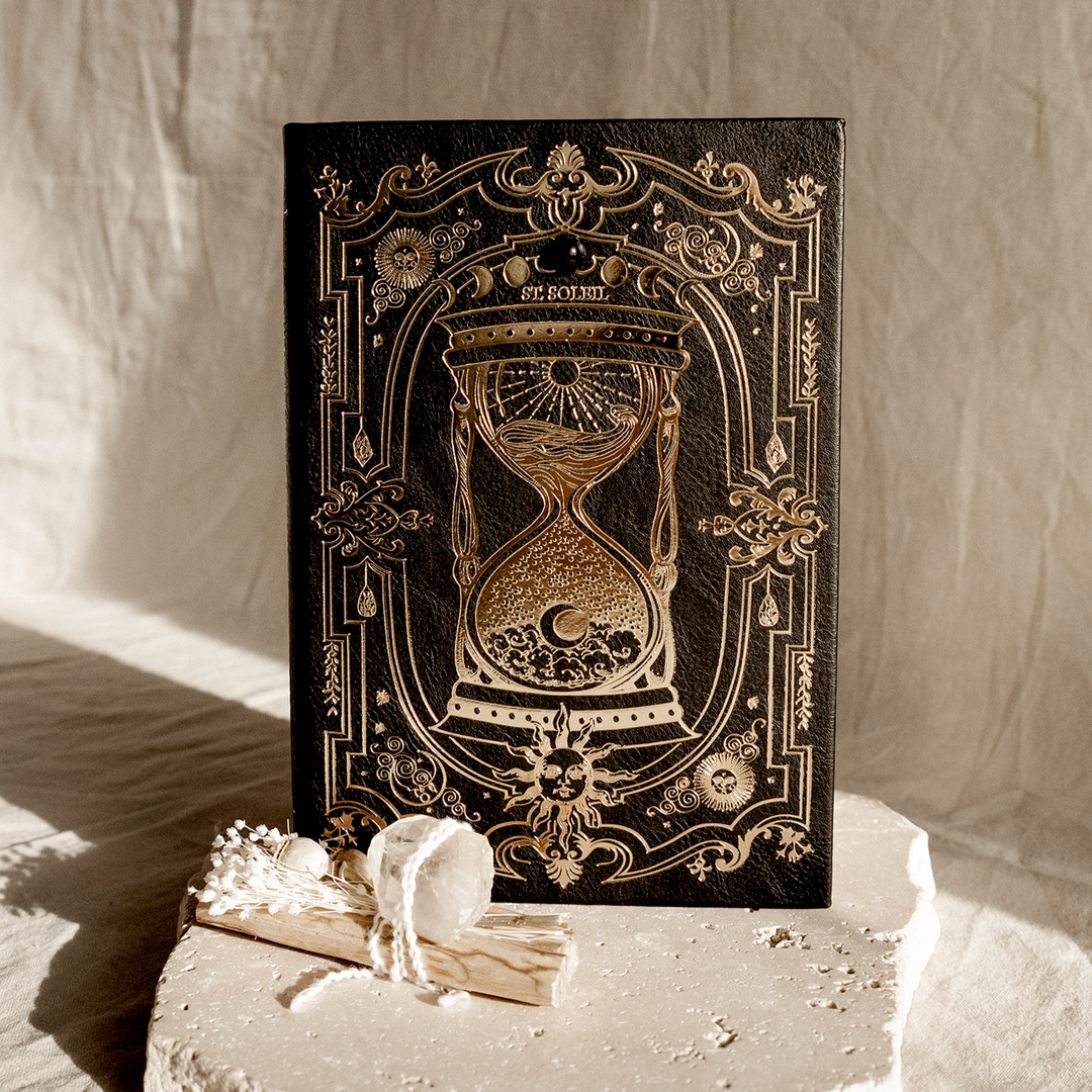 A vegan leather dream journal with gold foiling and a black obsidian crystal embedded on the cover, presented on a soft, light background with some plant elements.