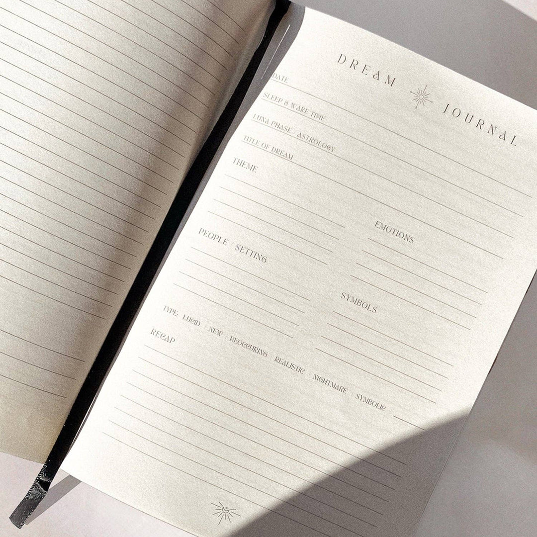 A vegan leather dream journal with gold foiling and a black obsidian crystal embedded on the cover, presented on a soft, light background with some plant elements.