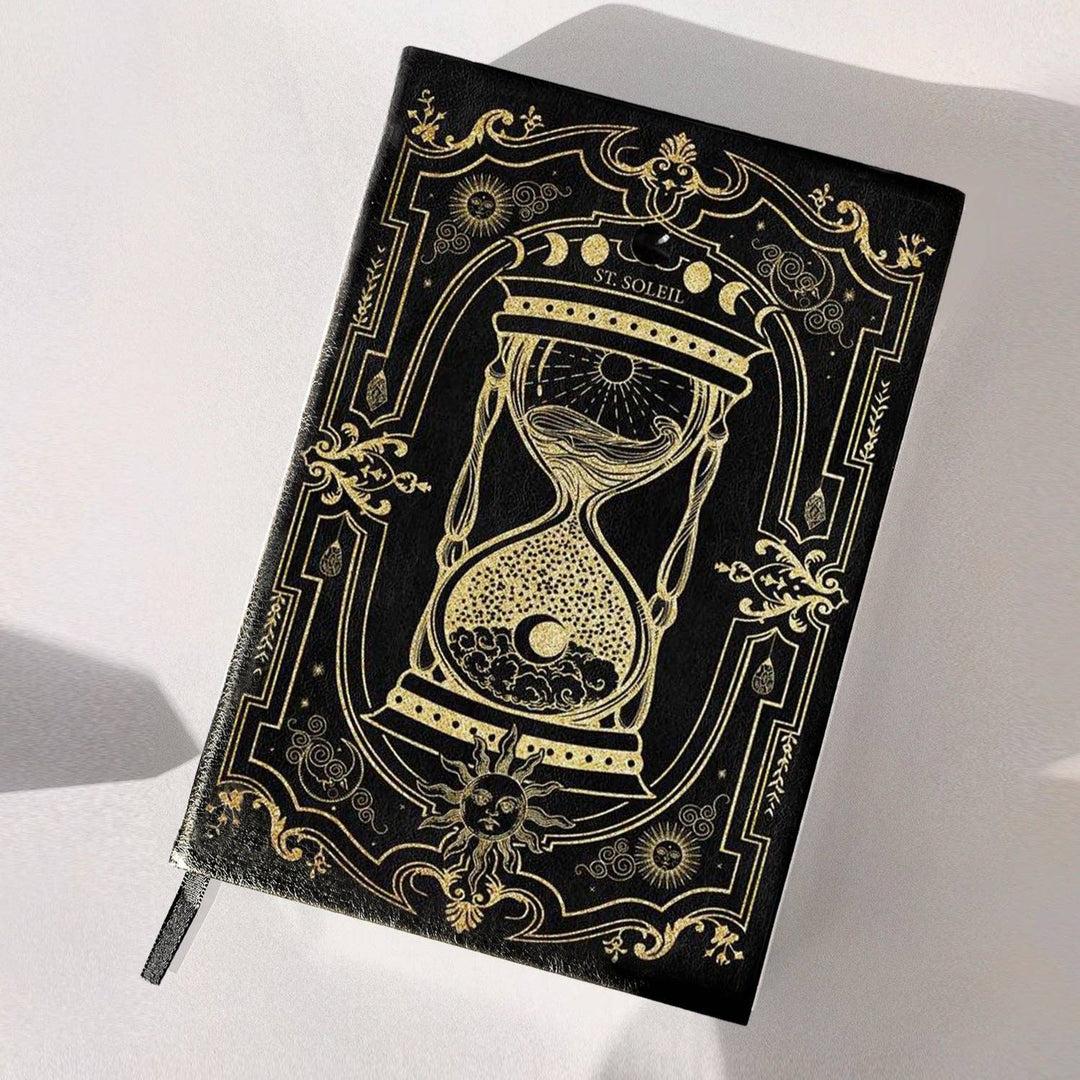 A vegan leather dream journal with gold foiling and a black obsidian crystal embedded on the cover, presented on a soft, light background with some plant elements.