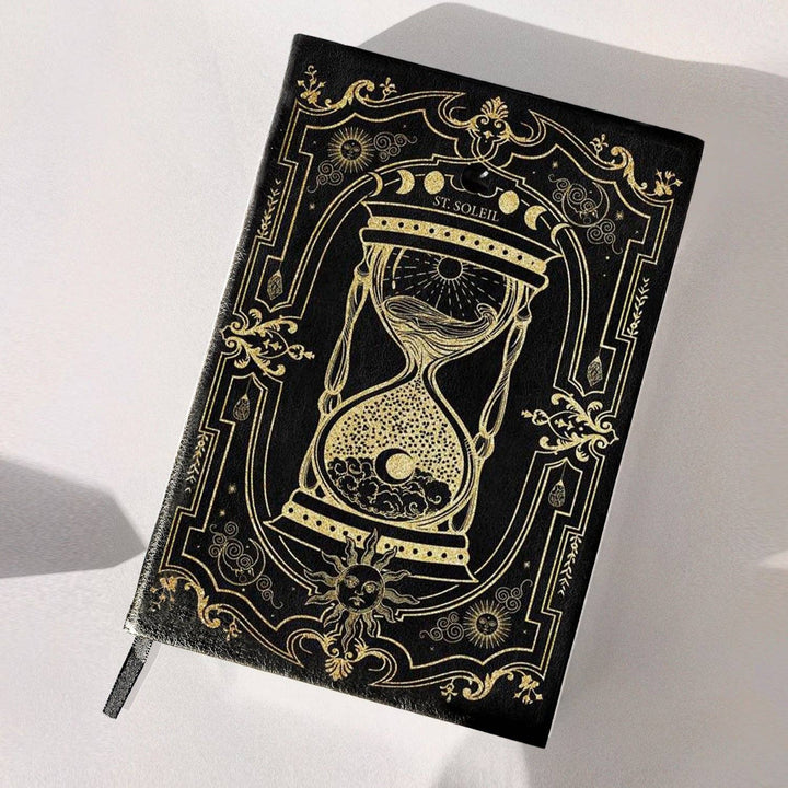 A vegan leather dream journal with gold foiling and a black obsidian crystal embedded on the cover, presented on a soft, light background with some plant elements.