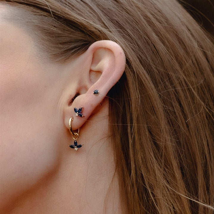 Close-up of a person wearing small earrings with butterfly designs.