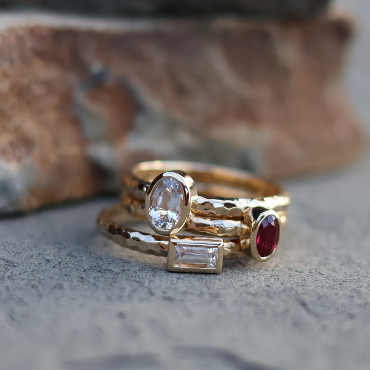 Gold rings stacked with gemstones on a textured surface