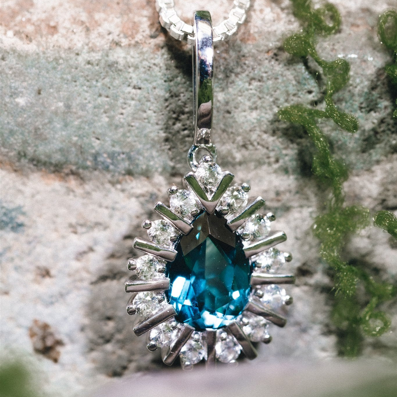 Silver pendant with a blue gemstone and clear stones on a textured surface