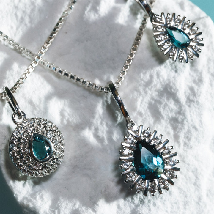 Two silver pendants with blue gemstones on a textured white surface