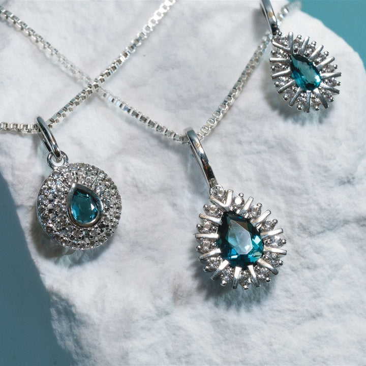Silver pendants with blue gemstones on a white stone surface