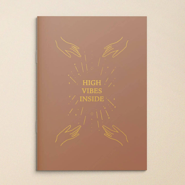 Brown book cover with gold text 'High Vibes Inside' and hand illustrations on a beige background