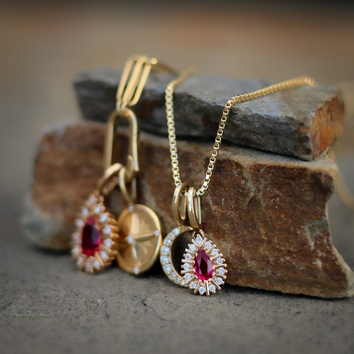 Gold jewelry set with pendants featuring red gemstones on a stone surface.