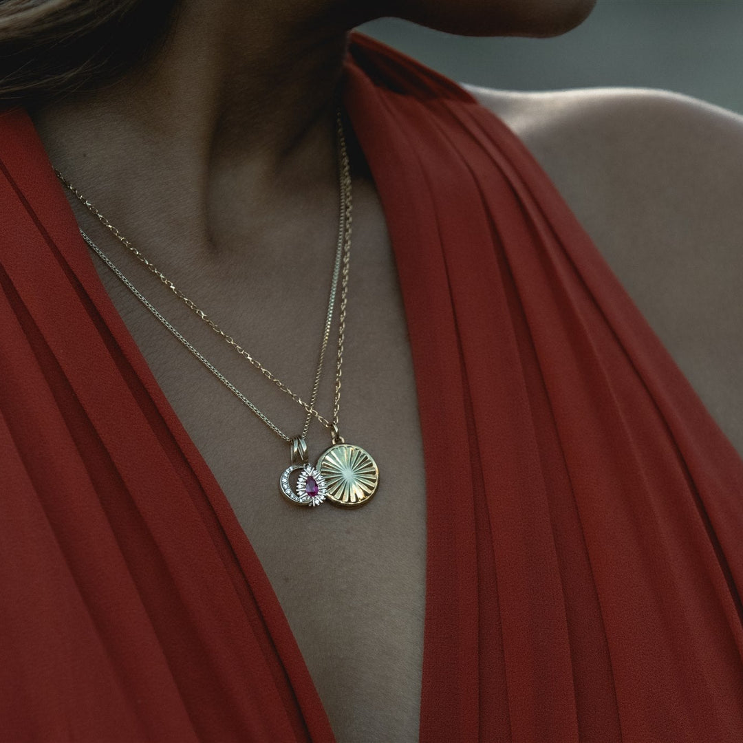 Close-up of a person wearing a gold necklace with a pendant, against a blurred background.