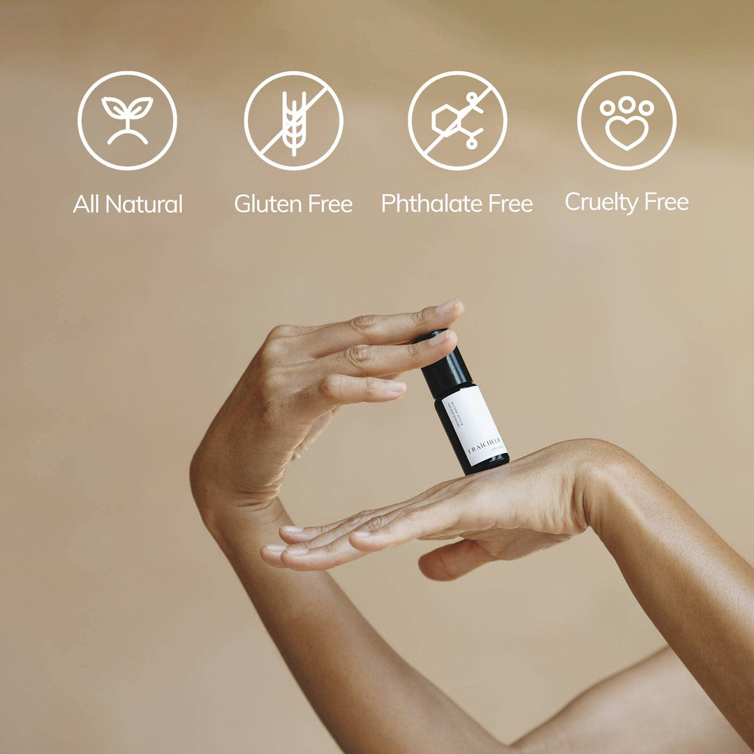 Hand holding a small bottle with certification icons for All Natural, Gluten Free, Phthalate Free, and Cruelty Free on a beige background.