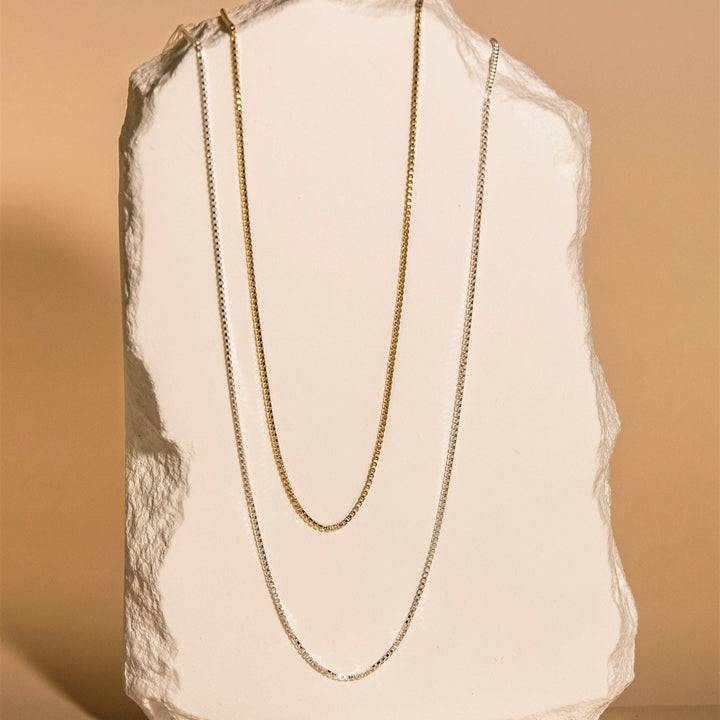 Gold chain necklace on a textured beige surface