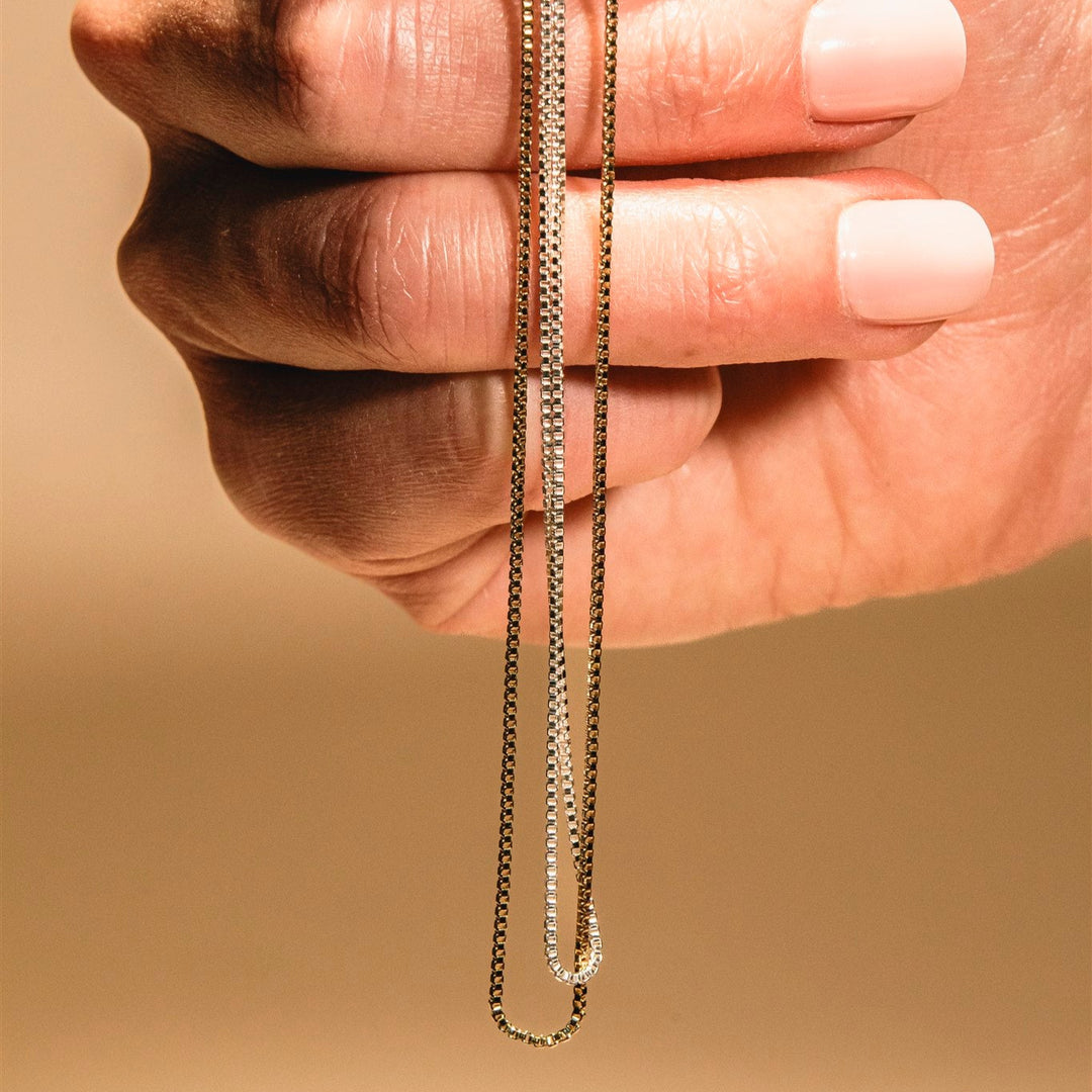 Hand holding a gold chain against a beige background