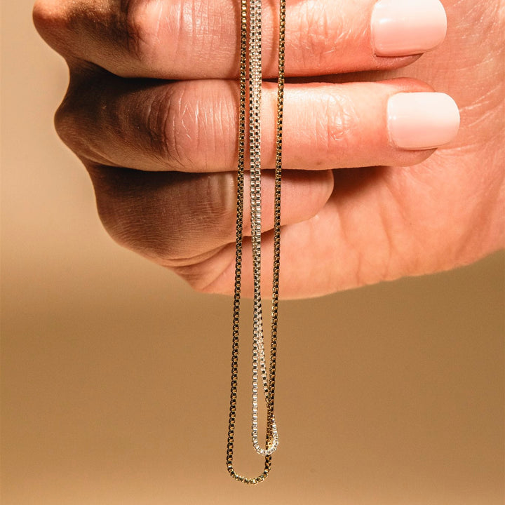 Hand holding a gold chain against a beige background