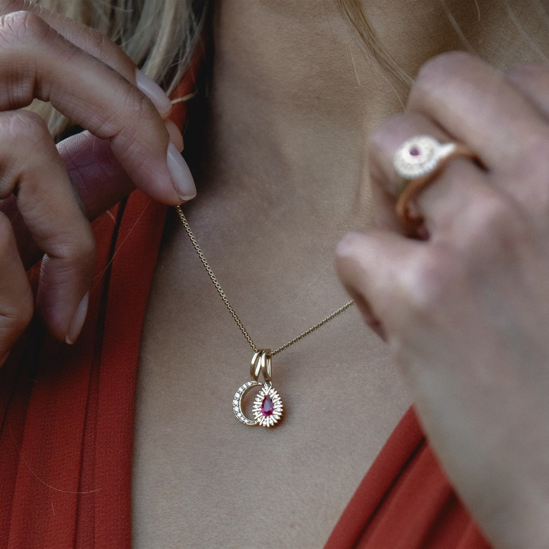 Close-up of a person wearing a gold necklace with a pendant, with a blurred background.