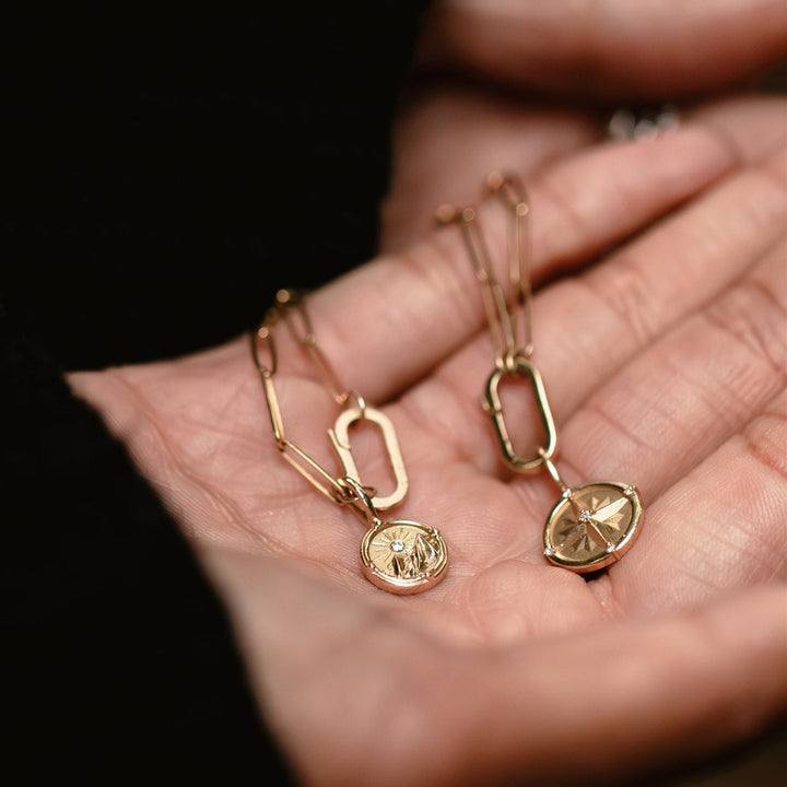 Gold necklaces with pendant charms held in a hand against a dark background