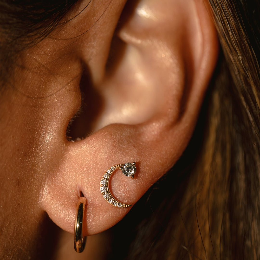 Close-up of an ear with gold hoop and diamond crescent moon earrings.