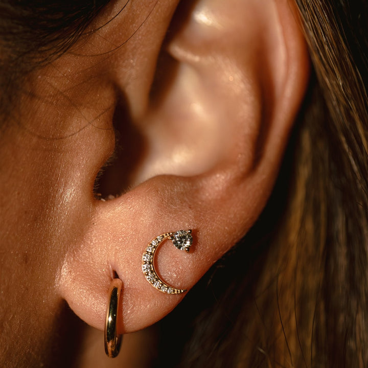 Close-up of an ear with gold hoop and diamond crescent moon earrings.