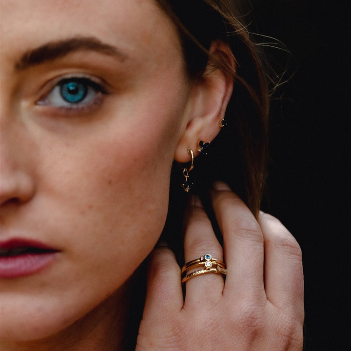 Close-up of a woman wearing gold earrings and rings against a dark background