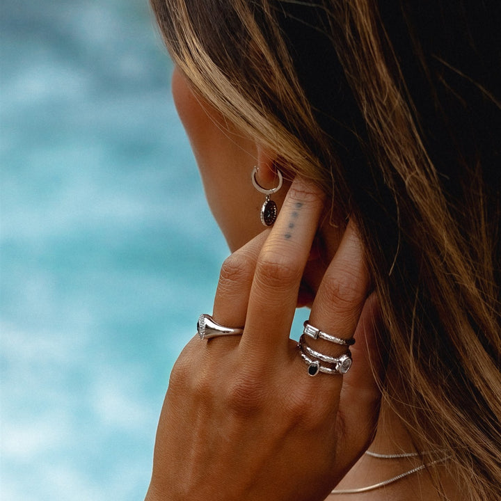 Close-up of a hand with multiple rings and earrings against a blurred natural background