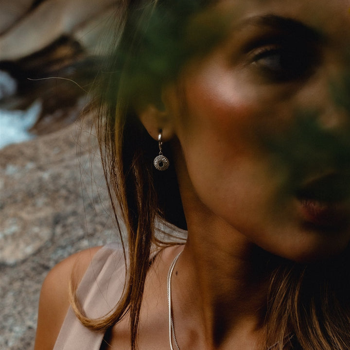 Close-up of a woman wearing necklaces and earrings with a blurred natural background