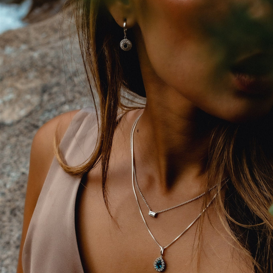 Close-up of a woman wearing necklaces and earrings with a blurred natural background