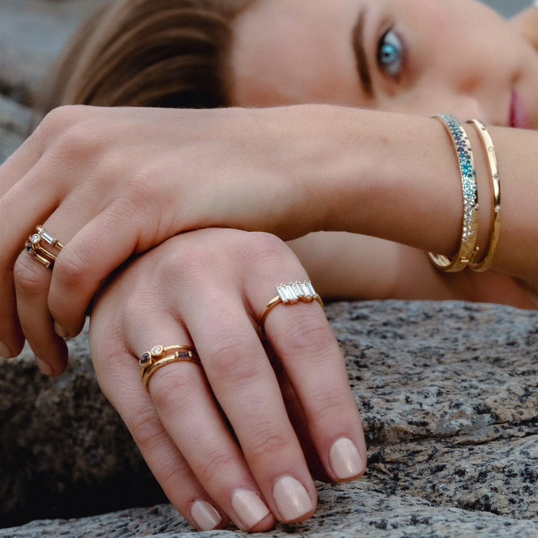 Close-up of hands with gold rings and bracelets on a rocky surface