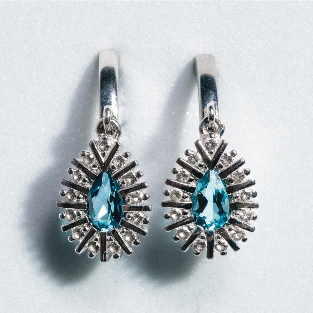 Pair of silver earrings with blue gemstones on a light gray background