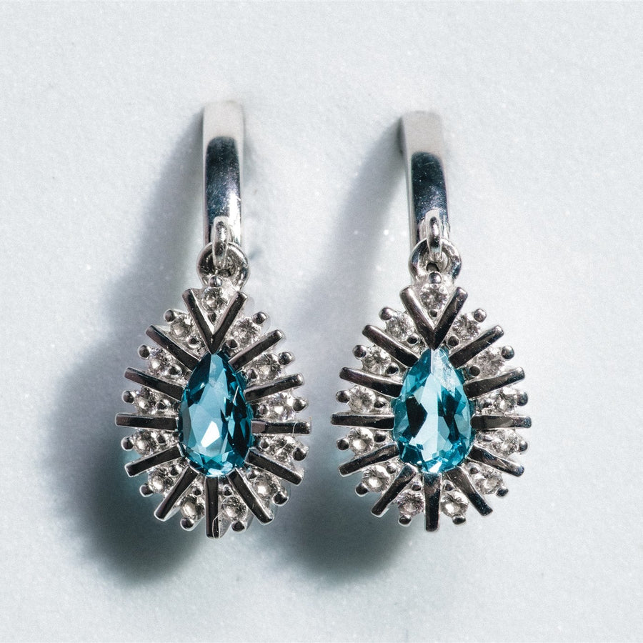 Pair of silver earrings with blue gemstones on a light gray background