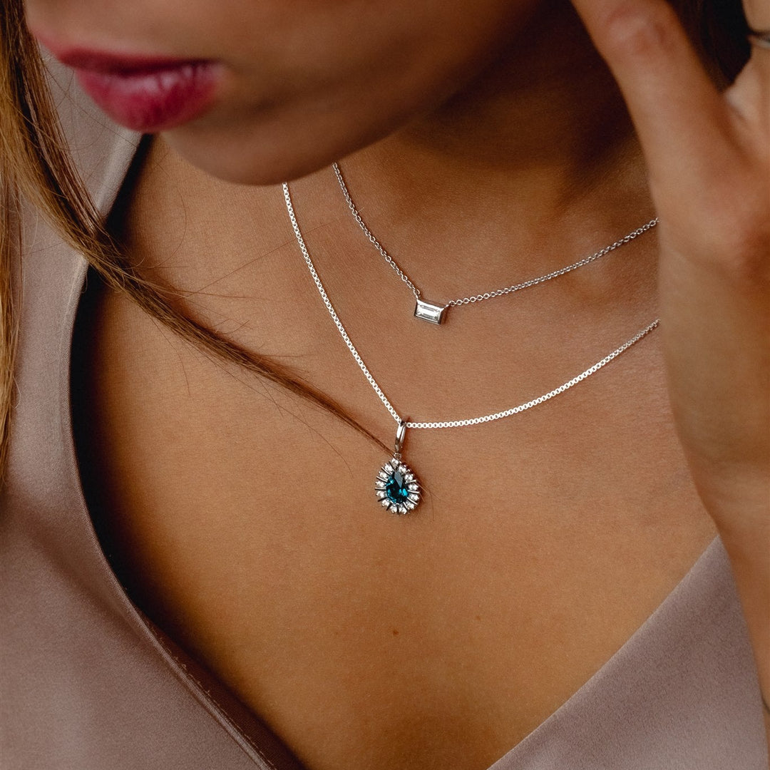 Close-up of a woman wearing a silver necklace with a blue gemstone pendant.