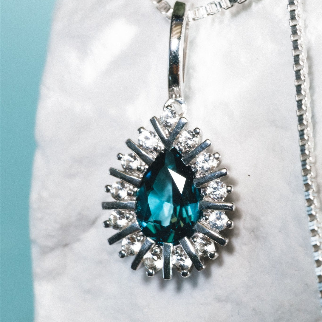Blue teardrop pendant with silver chain on a white marble surface