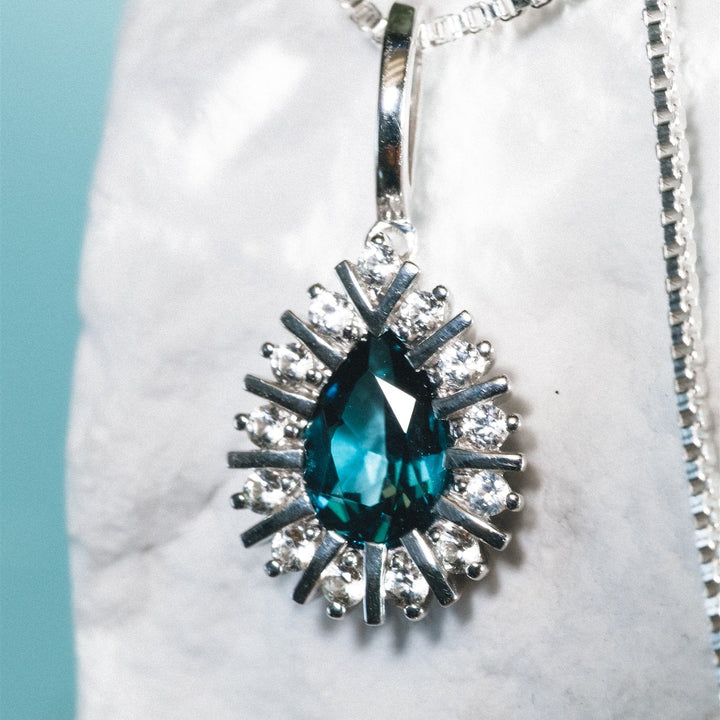 Blue teardrop pendant with silver chain on a white marble surface
