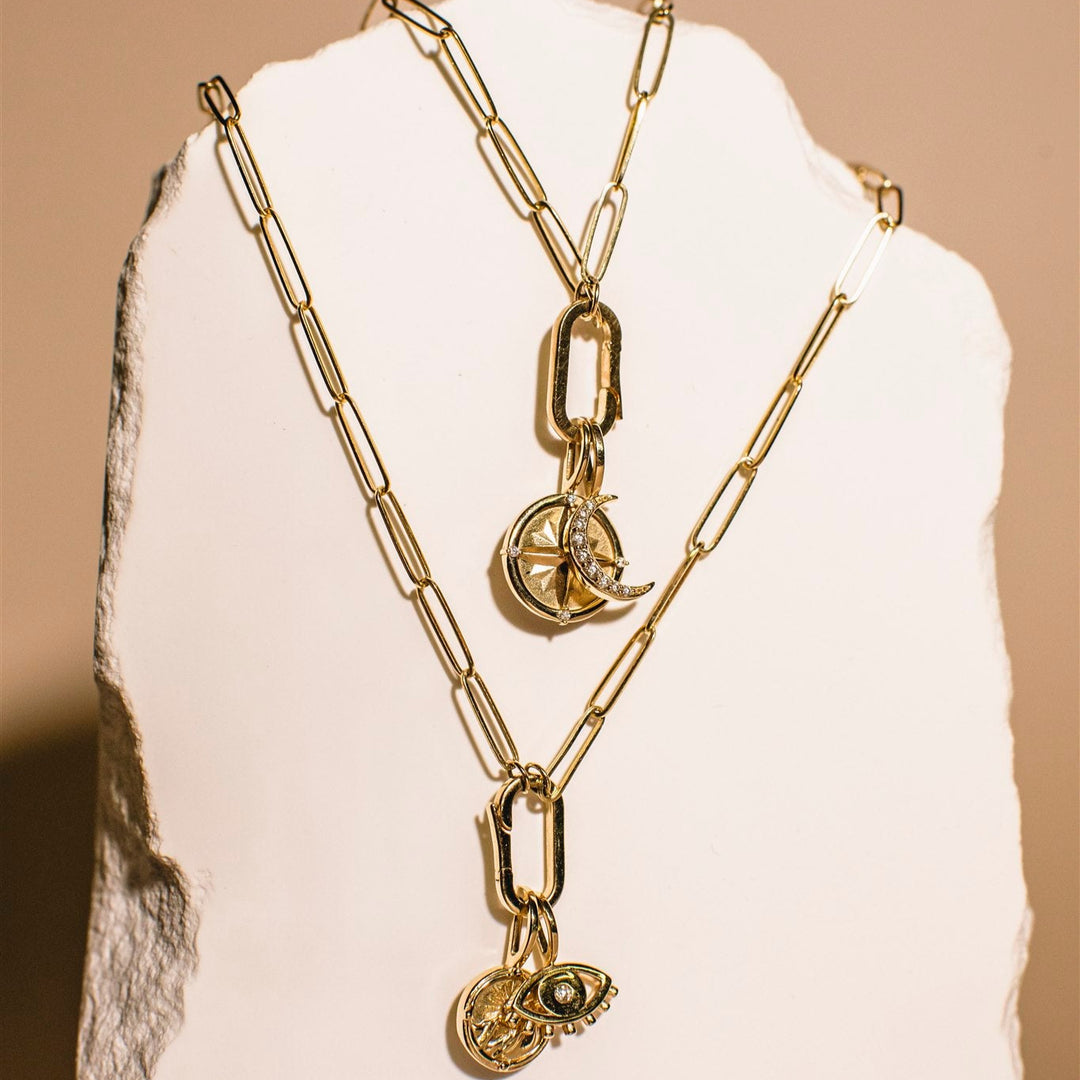 Gold chain necklaces with heart and round pendants on a white stone surface.