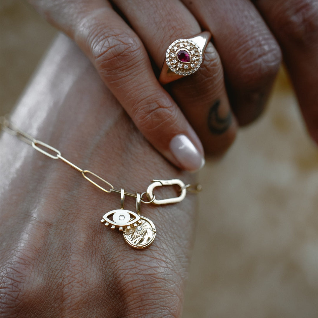Close-up of a hand wearing gold rings and a bracelet with charms on a blurred background
