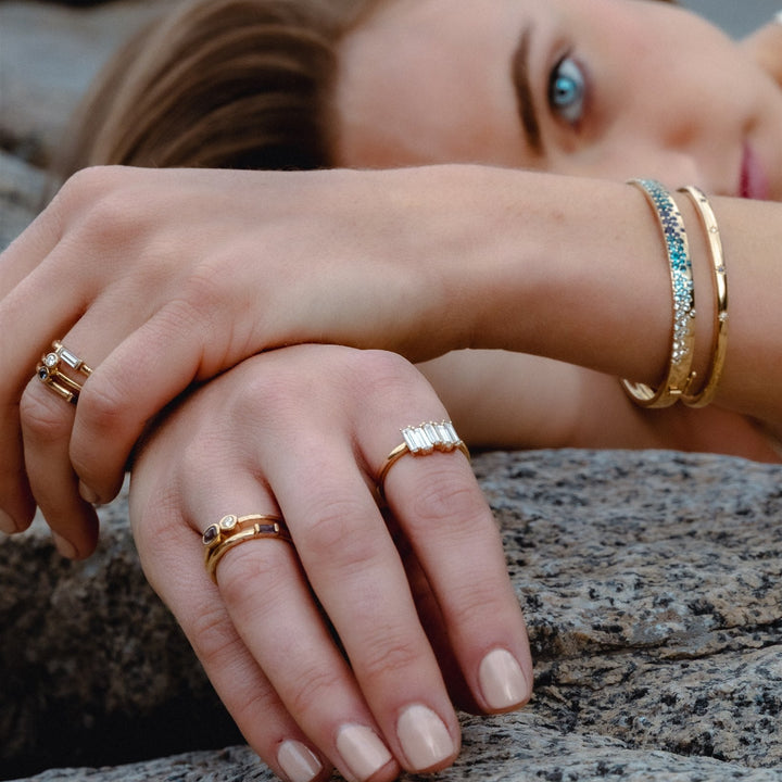 Close-up of hands with gold rings and bracelets on a rocky surface