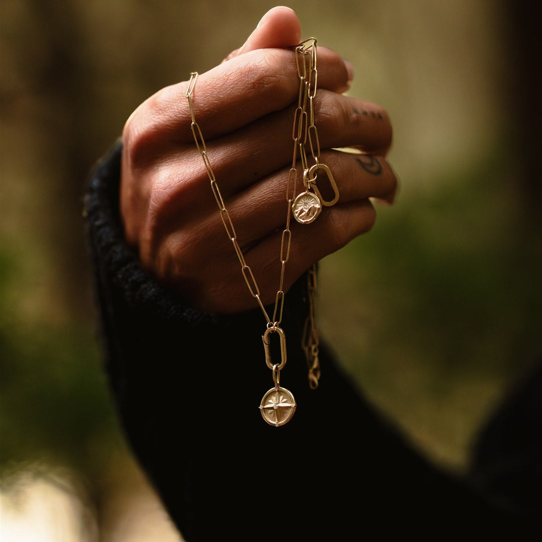 Hand holding a gold chain with pendants against a blurred natural background