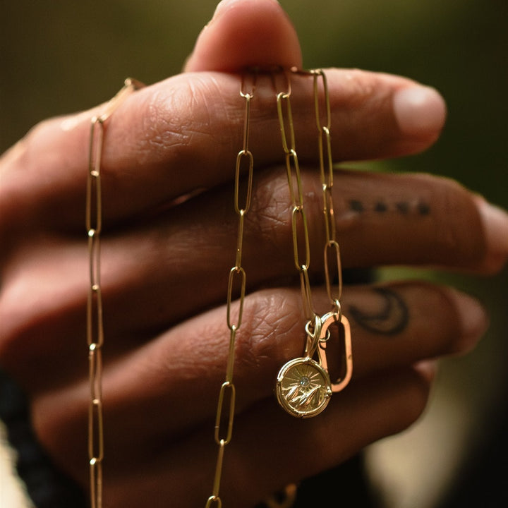 Gold chain necklace with a pendant held by a hand against a blurred background
