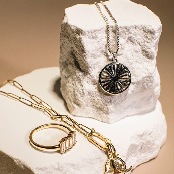 Jewelry set including a necklace, ring, and pendant on a textured white surface.