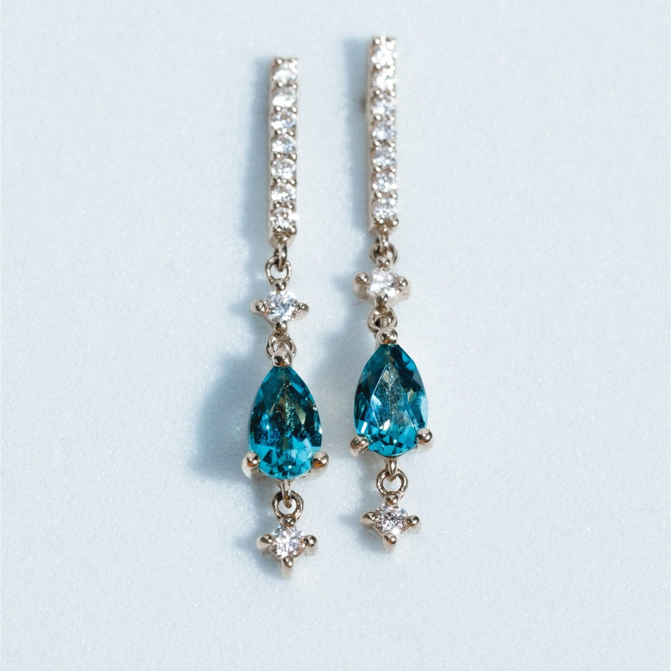 Pair of earrings with blue teardrop stones and clear gemstones on a light gray background