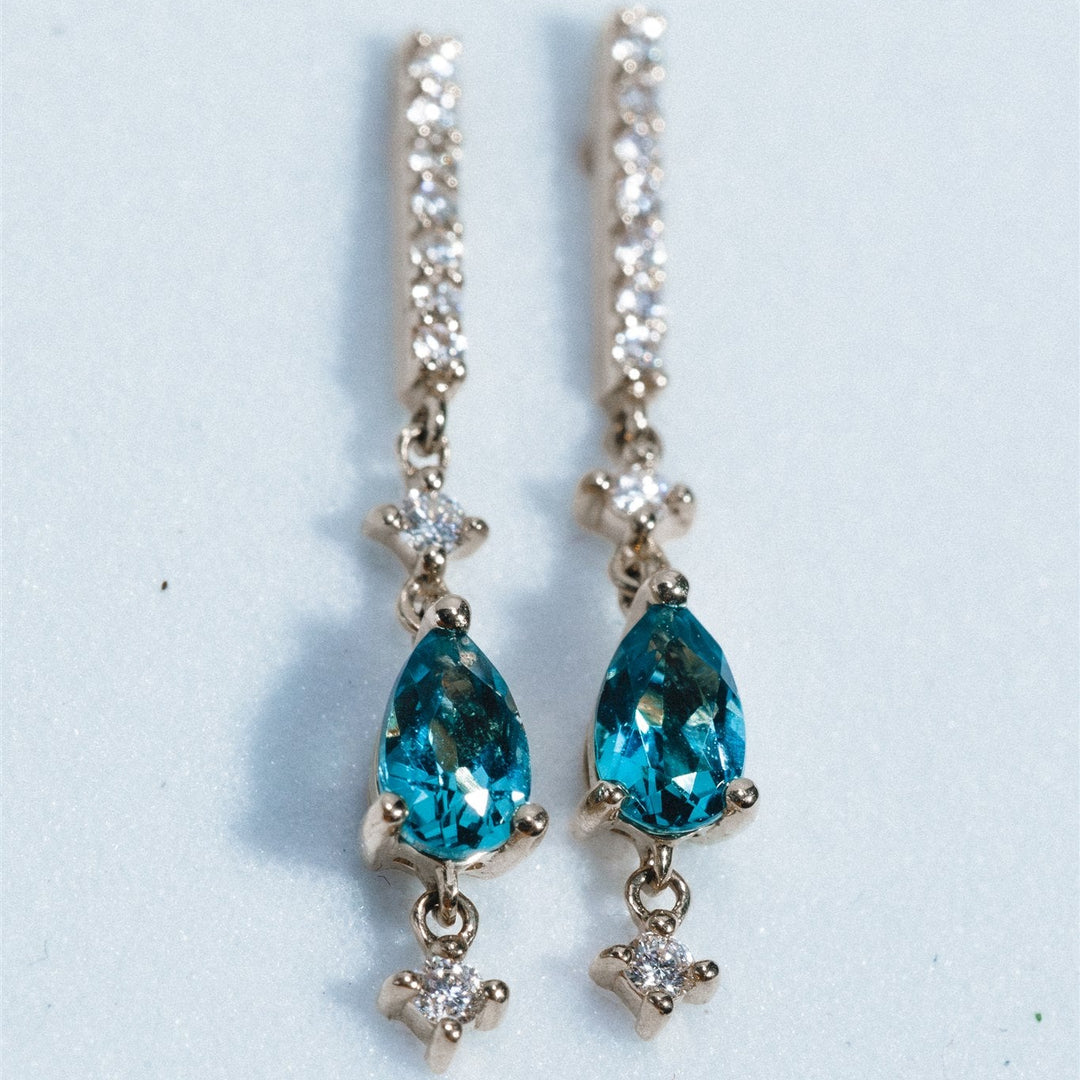 Pair of earrings with blue teardrop stones and gold accents on a light gray background