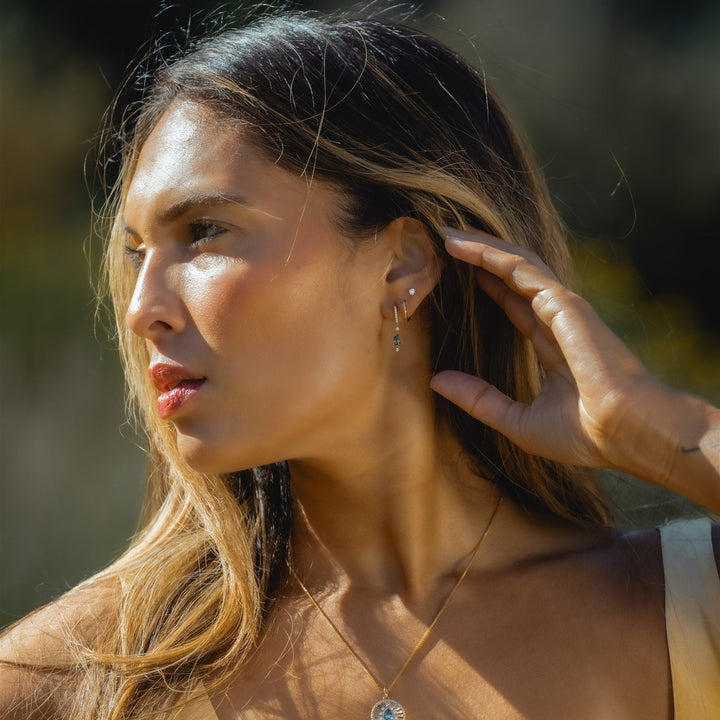 Woman adjusting her earring outdoors with a blurred natural background