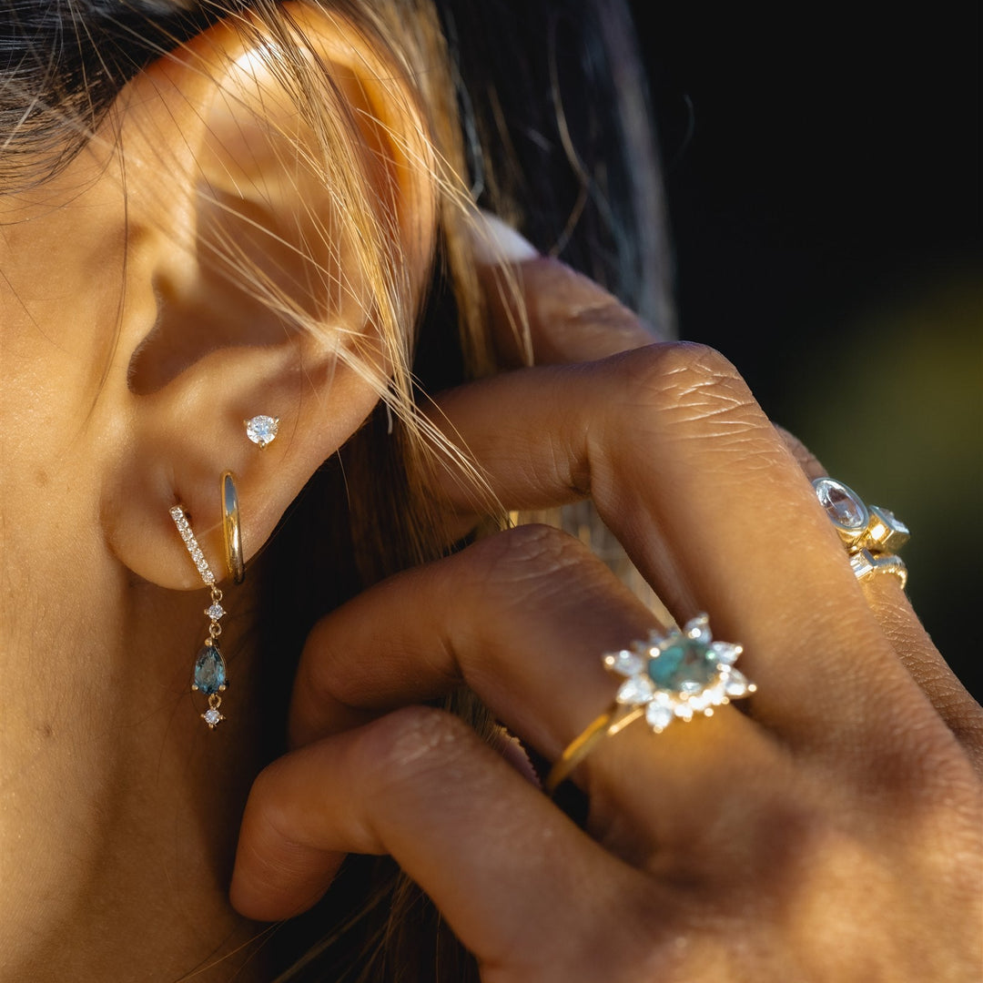 Close-up of a person wearing gold earrings and rings with gemstones.