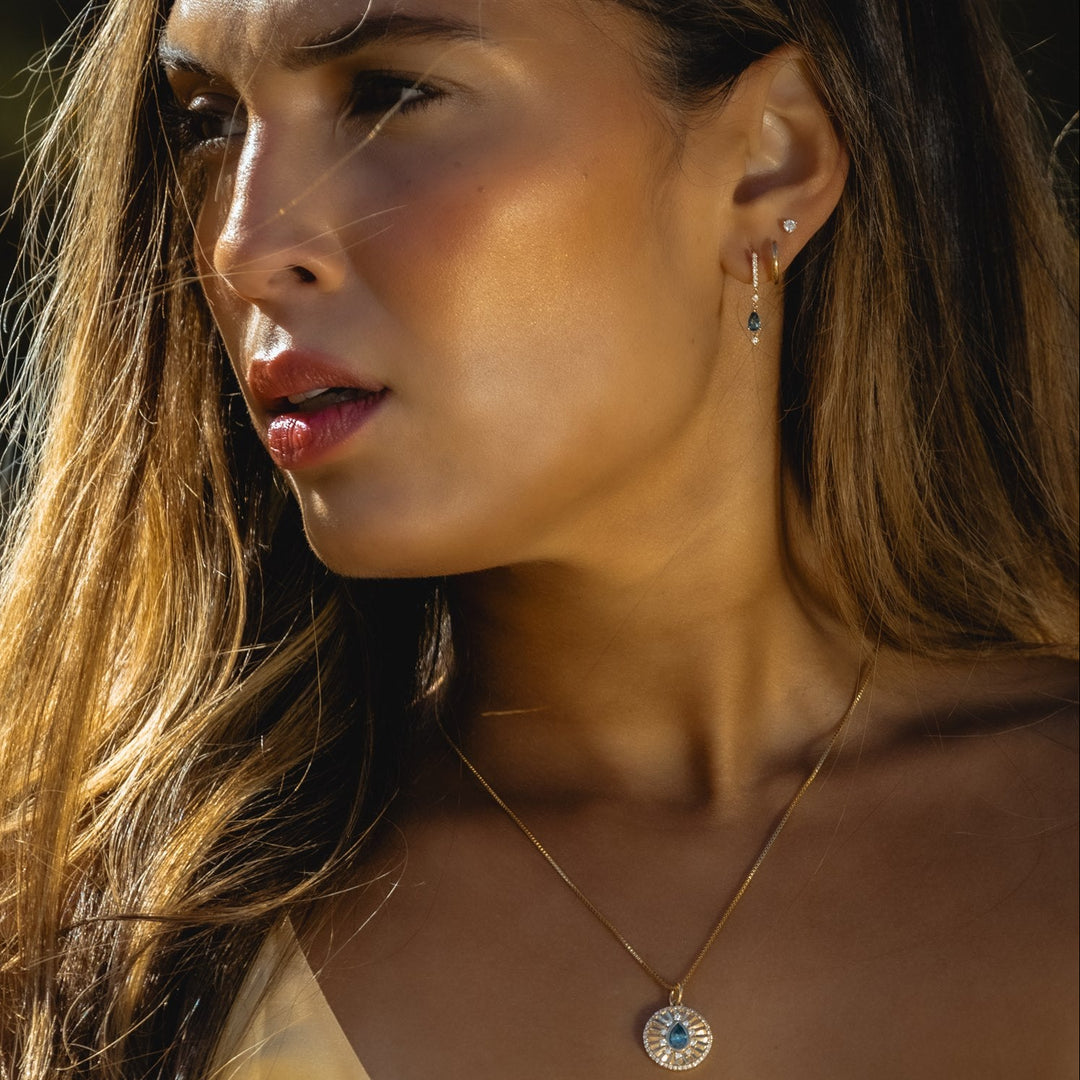Close-up of a woman wearing earrings and a necklace with a blue gemstone.