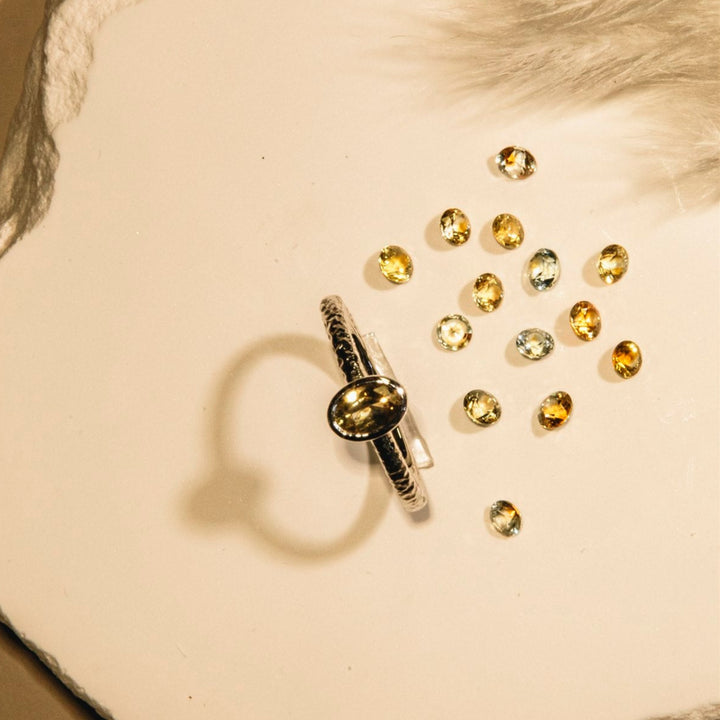 Gold ring with scattered gemstones on a textured beige surface