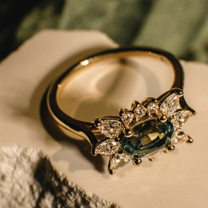Gold ring with a central gemstone and diamond accents on a textured surface.