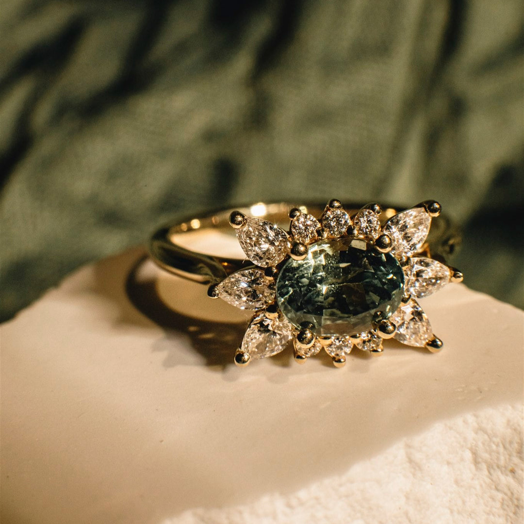 Gold ring with a green gemstone and diamond accents on a textured surface.