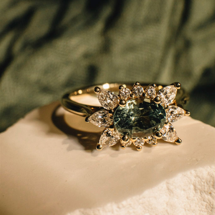 Gold ring with a green gemstone and diamond accents on a textured surface.